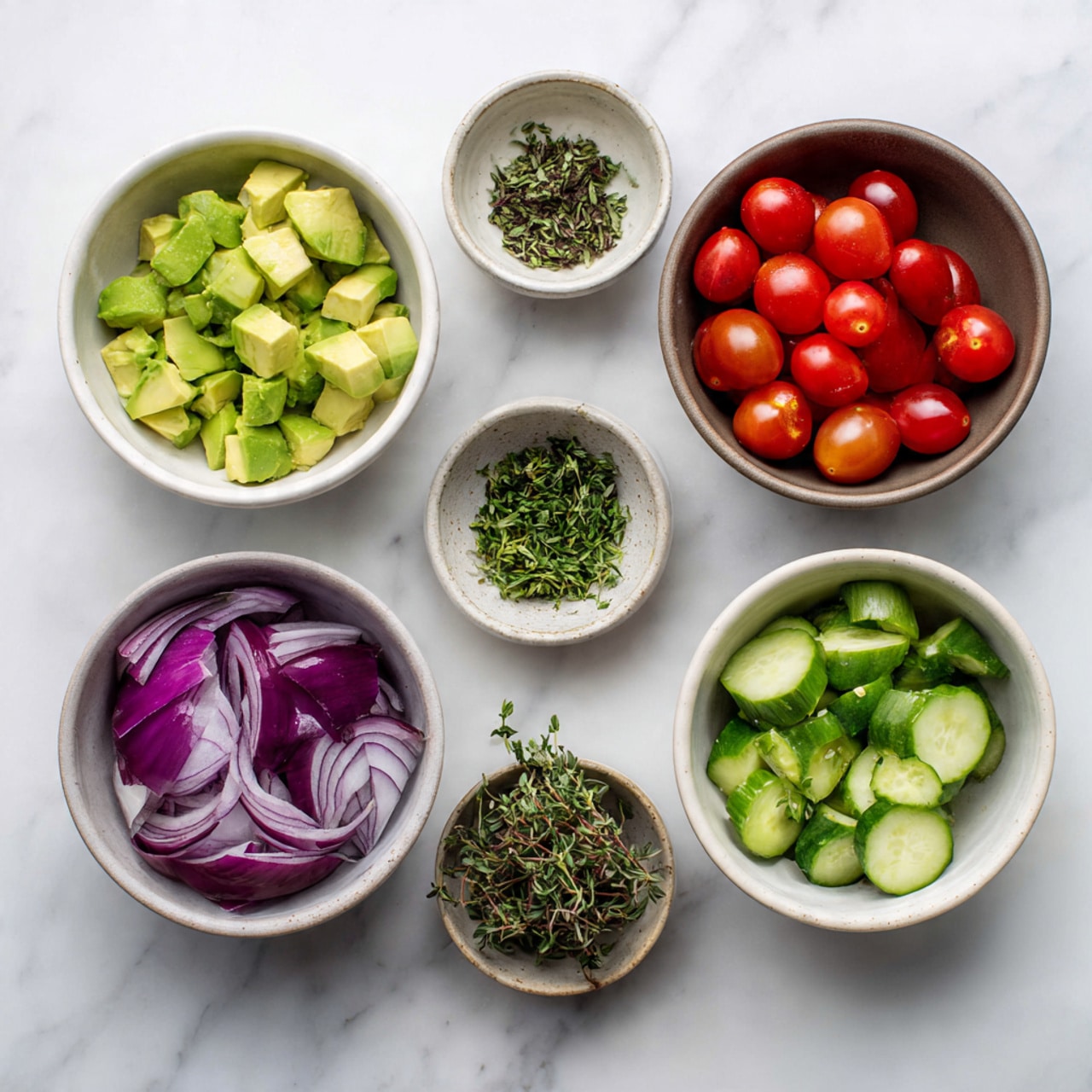 The image shows six white bowls with different fresh ingredients on a white marbled surface. Starting from the top left, there is a bowl filled with light green chunks of avocado. To the right, a bowl contains bright red cherry tomatoes with glossy skins. Below the avocado, a small bowl holds finely chopped fresh cilantro or parsley, and to its right another small bowl contains additional fresh herbs. At the bottom left, a bowl holds sliced purple-red onions with white layers showing, and the last bowl on the bottom right contains light green cucumber slices with darker green edges and a moist texture. Photo taken with an iphone