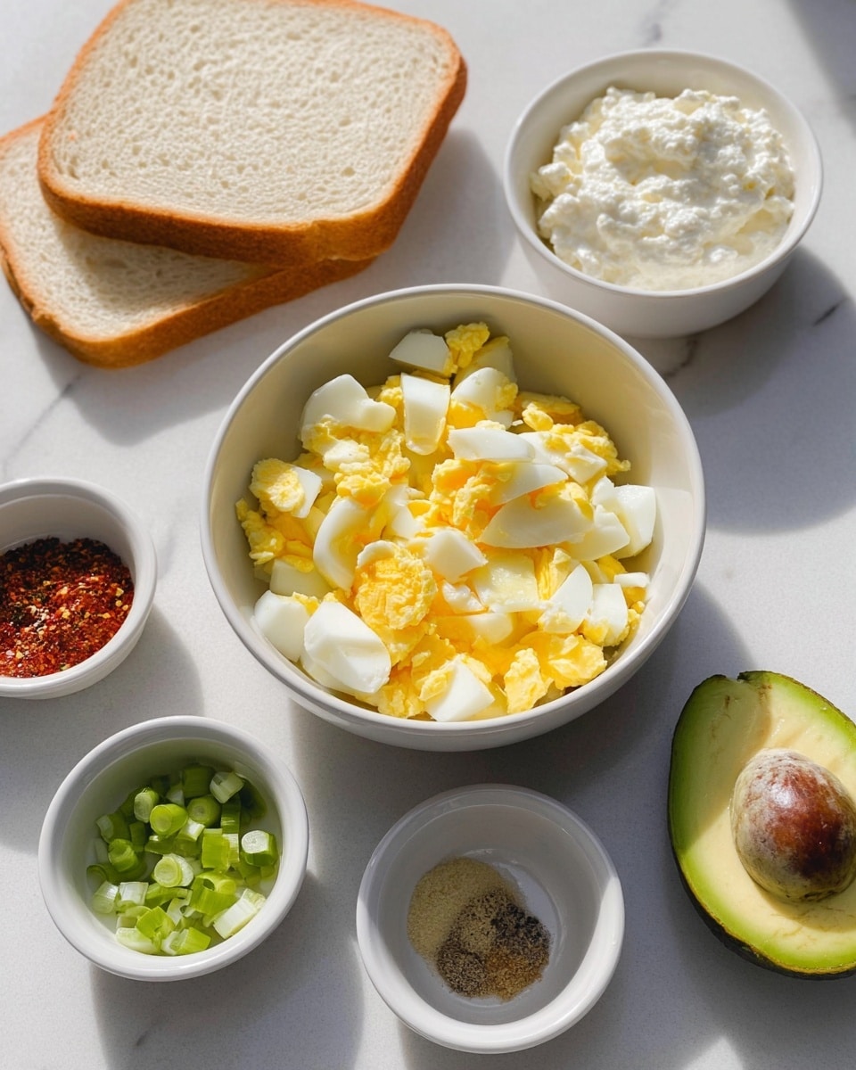 The image shows a white bowl in the center filled with chopped hard-boiled eggs that have yellow yolks and white whites. Behind it is a slice of light brown bread with a soft texture, resting on a white marbled surface. To the back right is a white bowl with a creamy white mixture that looks like cottage cheese. Around the main bowl are small white ramekins holding chopped green onions, whole grain mustard, and a mix of red and black spices. In the front right corner is half of a ripe avocado with a green inside and a brown pit, placed on the white marbled surface. The light shines naturally from the left side, creating soft shadows. photo taken with an iphone --ar 4:5 --v 7