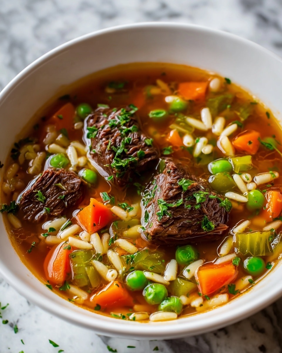 A white bowl filled with beef soup showing about three large chunks of dark brown beef on top. Around the beef are many small pieces of bright orange carrots, light green celery, and green peas. There are also small, white, rice-shaped pasta pieces mixed evenly throughout the light brown broth. The soup is sprinkled with finely chopped fresh green herbs. The bowl sits on a white marbled surface. Photo taken with an iphone --ar 4:5 --v 7