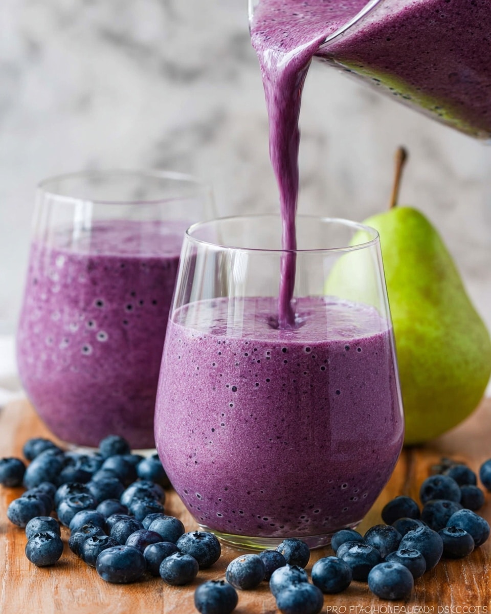A close-up shot shows a thick purple smoothie being poured into a clear round glass, filling it almost to the top with tiny bubbles on the surface; behind it is a second glass also filled with the same purple smoothie. Around the glasses, fresh whole blueberries are scattered on a light wooden surface, with a whole green pear placed to the right side. The background is changed to a white marbled texture. Photo taken with an iphone --ar 4:5 --v 7