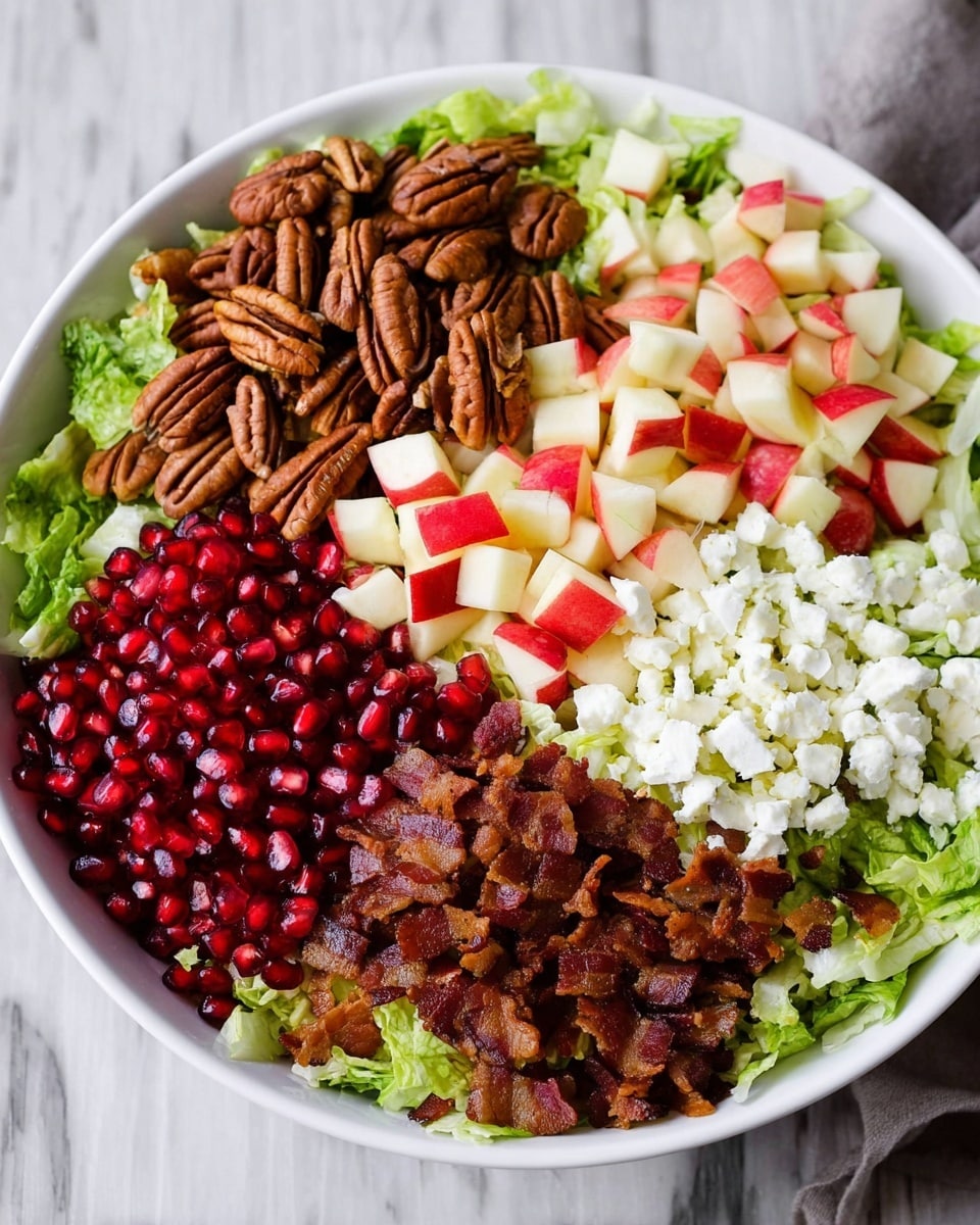 A white bowl filled with a colorful salad sitting on a white marbled surface. The base is shredded green lettuce visible around the edges. On top, there are five main layers arranged side by side: a pile of brown pecan halves on the left, next to diced red and white apple pieces in the middle, followed by white crumbled cheese on the right. Below the apples and cheese are bright red pomegranate seeds on the left and crispy small brown bacon pieces on the right. The colors and textures are vivid and fresh, showing a mix of crunchy, juicy, and soft ingredients. Photo taken with an iphone --ar 4:5 --v 7
