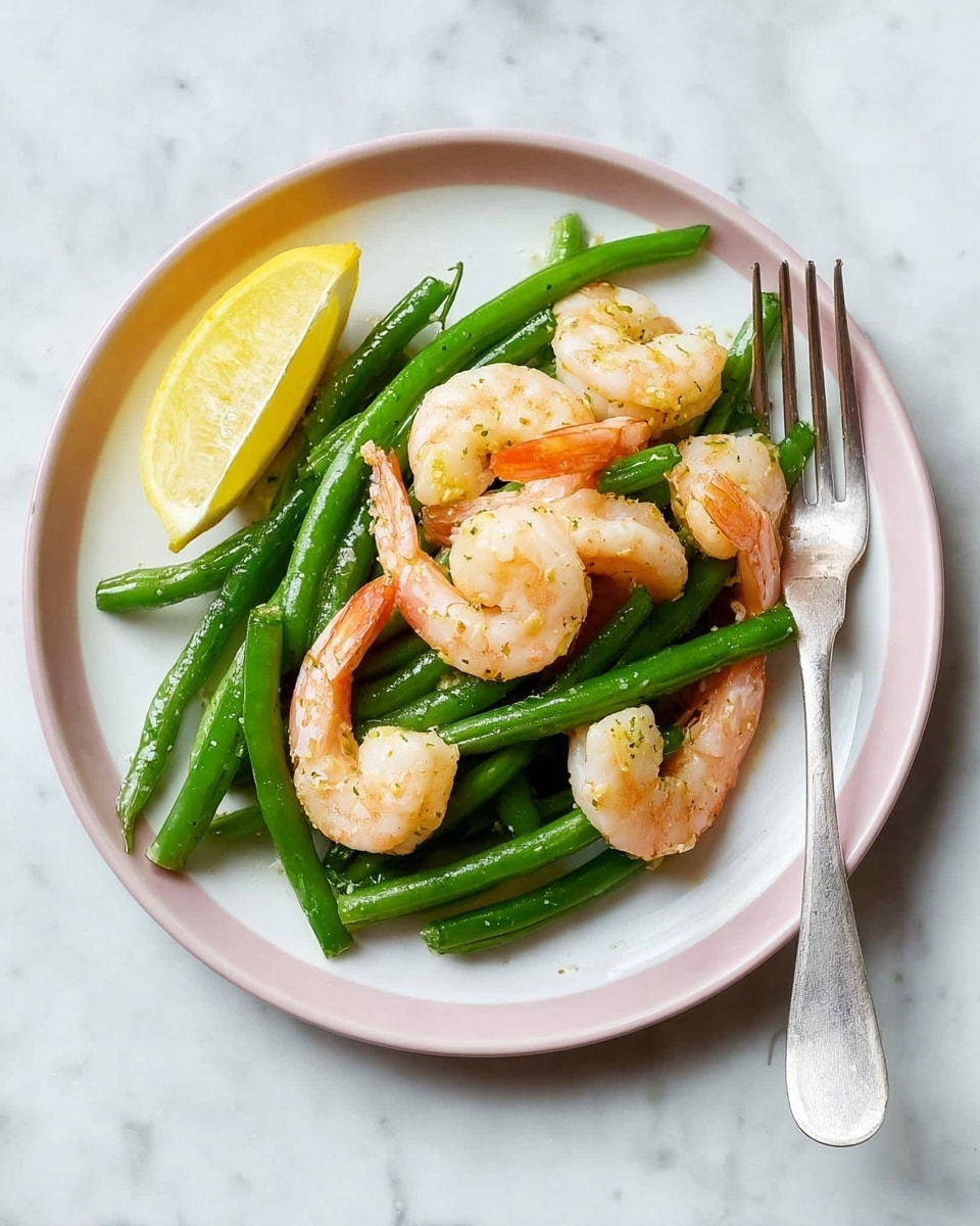 The image shows a white plate with a light pink rim, holding a simple dish made of green beans and four cooked shrimp arranged on top. The green beans are bright green and slightly shiny, forming the bottom layer, while the shrimp are a light orange and white, curled and placed over the beans. A yellow lemon wedge is positioned at the edge of the beans. There is a silver fork resting on the right side of the plate. The entire scene sits on a white marbled surface. Photo taken with an iphone --ar 4:5 --v 7